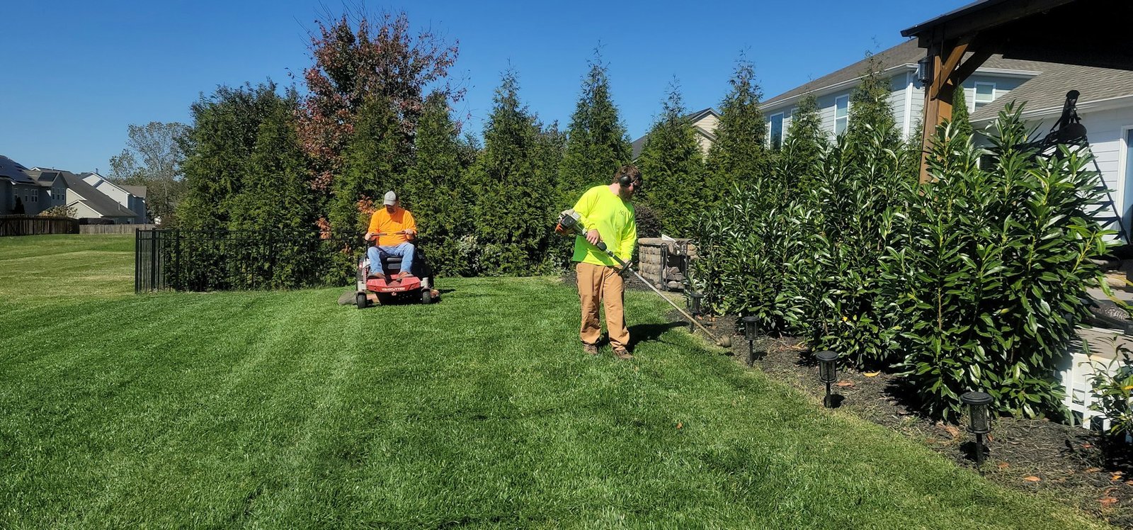 Landscaping crew mowing and trimming a residential lawn